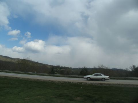 1995 Ford C-350 (Centurion Conversions) - A sedan travels down the road on a cloudy day, with rolling hills in the distance.