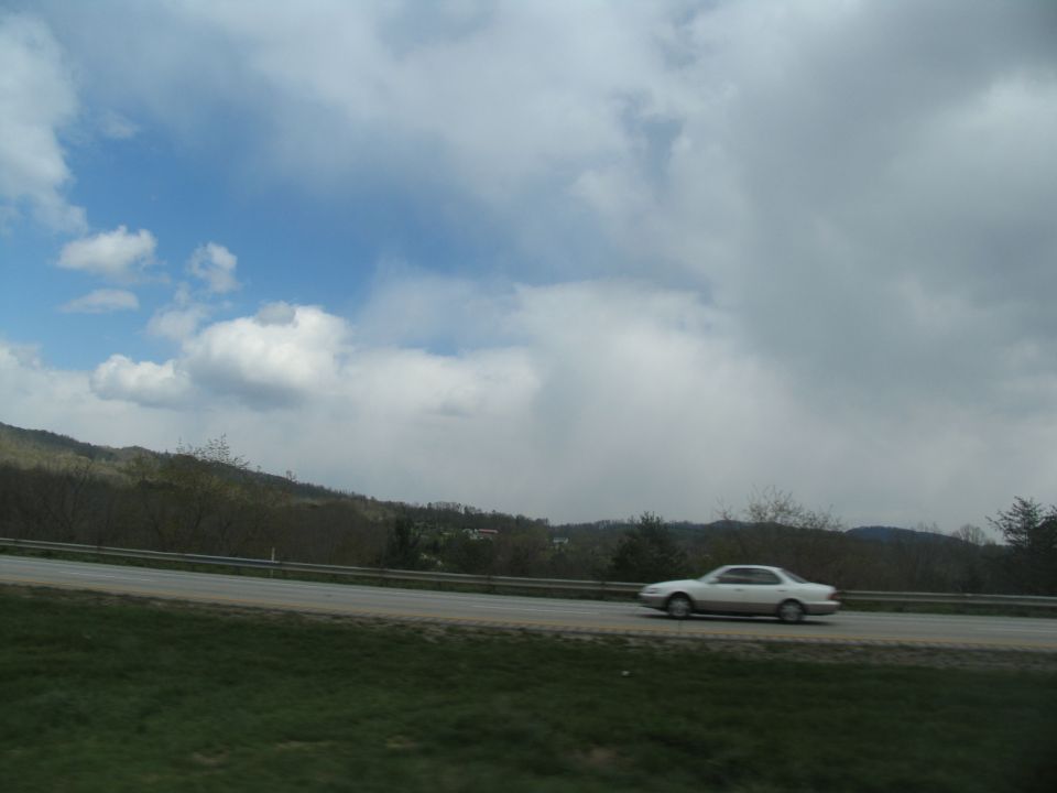 Car driving on a highway with hills and clouds in the background