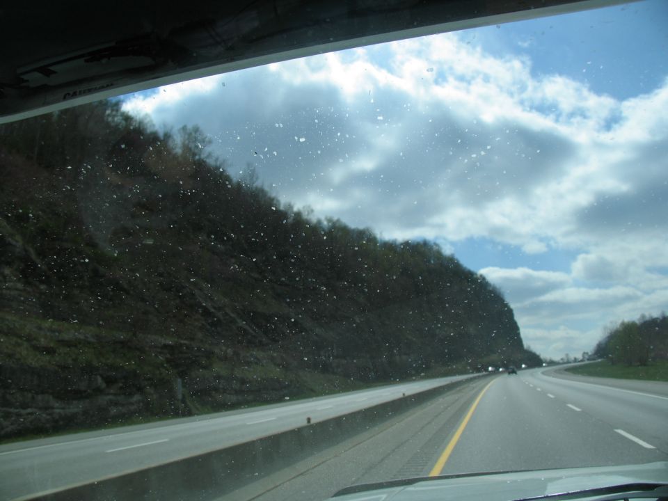 View from inside a vehicle looking out at a highway with trees and clouds