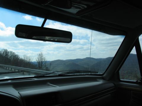 1995 Ford C-350 (Centurion Conversions) - View from inside a vehicle, showing the dashboard and windshield with a backdrop of rolling hills and a cloudy sky.
