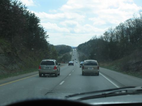 1995 Ford C-350 (Centurion Conversions) - View from inside a vehicle traveling on a highway with trees and hills on either side.
