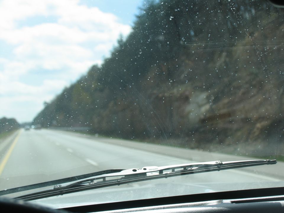 Windshield view from inside a vehicle looking out at a highway with trees and a rocky hill on the right