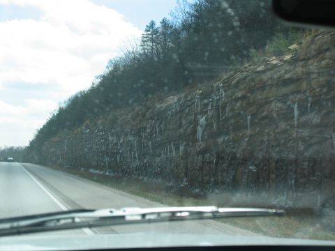 1995 Ford C-350 (Centurion Conversions) - A view of a rocky cliff face with icicles hanging down, seen from the perspective of a vehicle driving on a road.