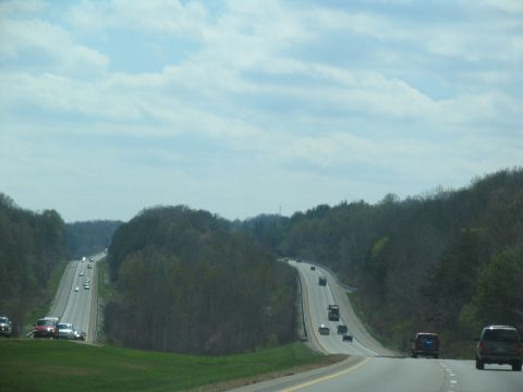 1995 Ford C-350 (Centurion Conversions) - Vehicles travel along a highway surrounded by trees and rolling terrain under a cloudy sky.