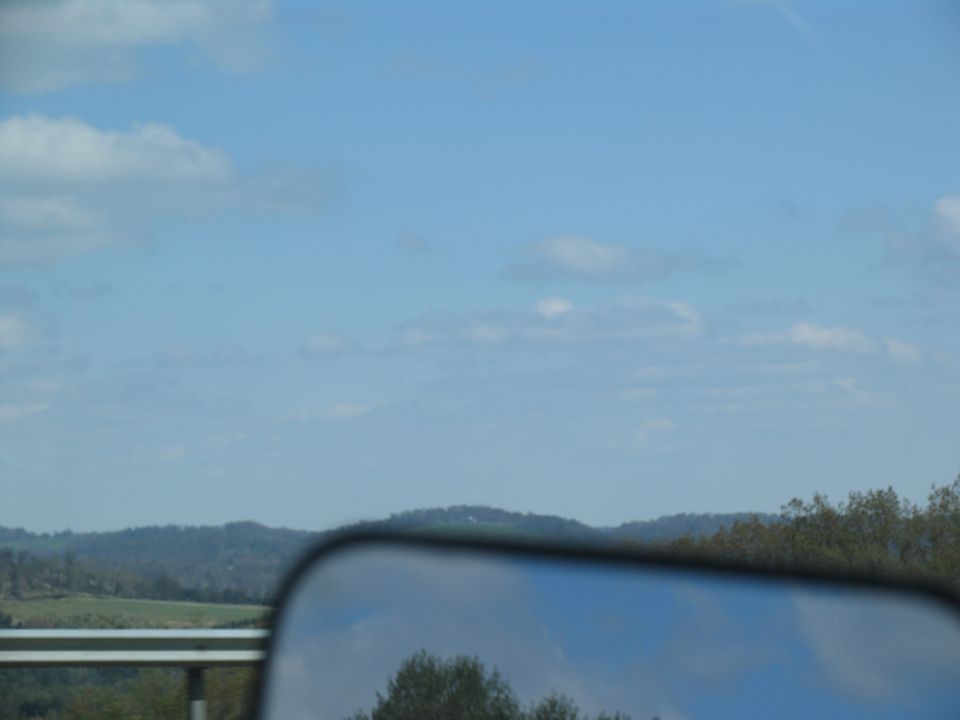 Side mirror reflection shows trees and blue sky with clouds
