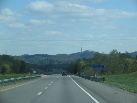 1995 Ford C-350 (Centurion Conversions) - A car drives down a highway with rolling hills and trees in the background under a cloudy sky.