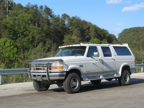 1995 Ford C-350 (Centurion Conversions) - Silver four-door SUV with a custom conversion, parked on a road with trees in the background.