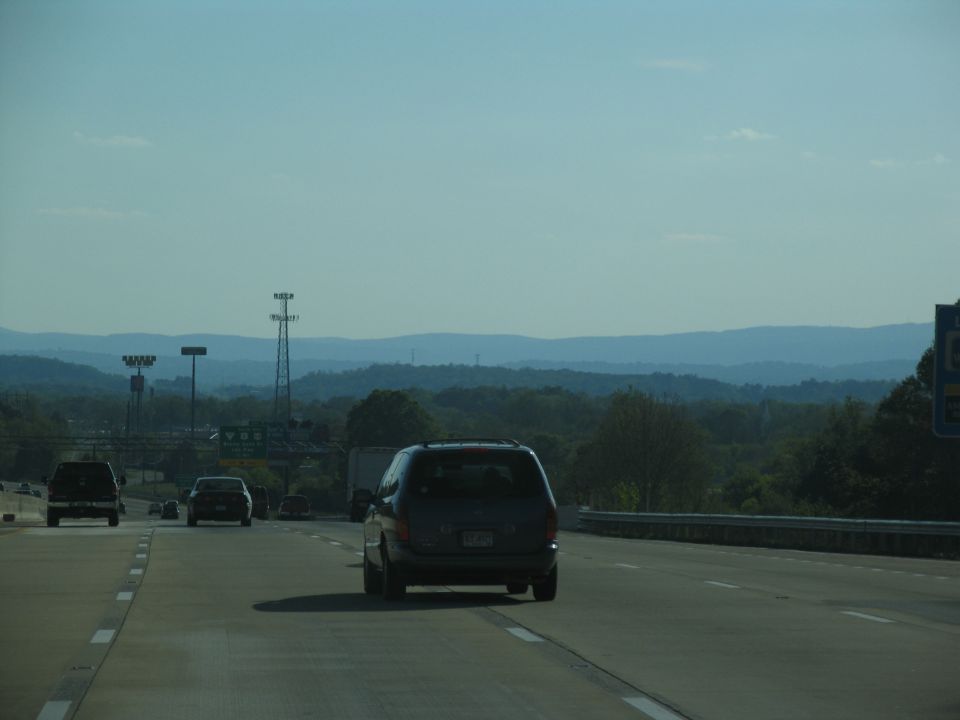 Minivan driving on highway with other cars and distant hills