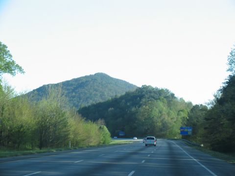 1995 Ford C-350 (Centurion Conversions) - A white van travels down a highway surrounded by trees and mountains under a clear sky.