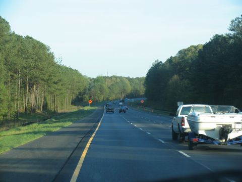 1995 Ford C-350 (Centurion Conversions) - A white pickup truck tows a boat trailer down a highway lined with trees.