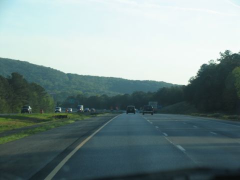1995 Ford C-350 (Centurion Conversions) - View from a car driving on a highway with other vehicles and a wooded hillside.