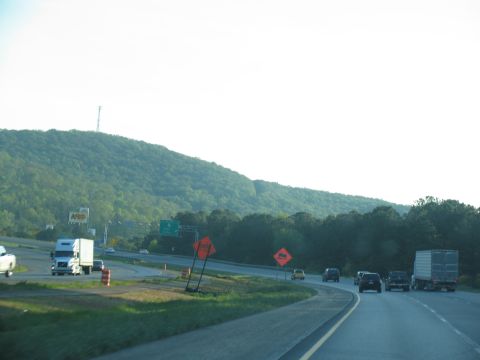 1995 Ford C-350 (Centurion Conversions) - Multiple vehicles travel on a highway with a large hill in the background and construction signs.