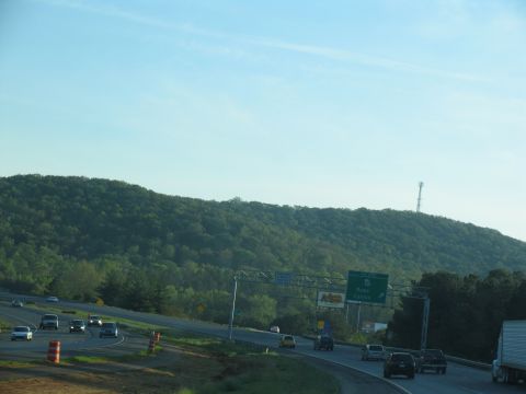 1995 Ford C-350 (Centurion Conversions) - Traffic moves along a highway with a large, green, wooded hill in the background under a bright blue sky.