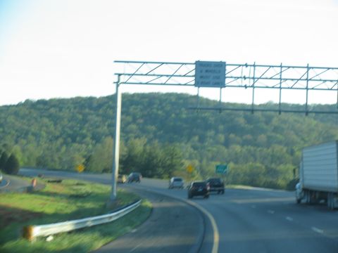 1995 Ford C-350 (Centurion Conversions) - Cars and a truck travel on a highway with wooded hills in the background.