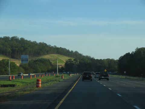 1995 Ford C-350 (Centurion Conversions) - Traffic moves along a highway under a clear blue sky, with construction barrels lining the shoulder.