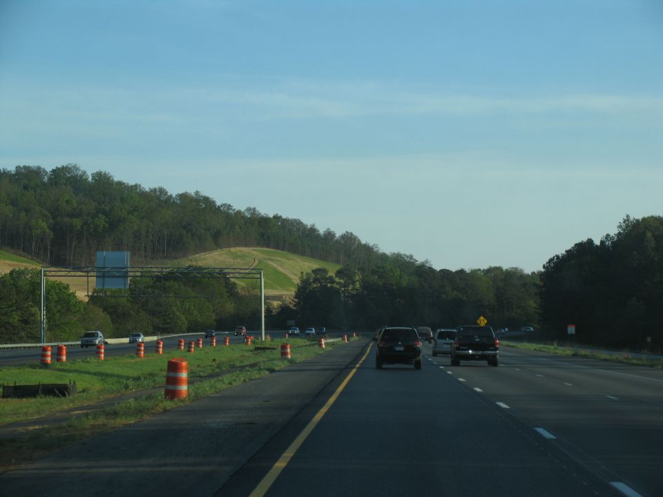 Cars driving on a highway with trees and a hill in the background