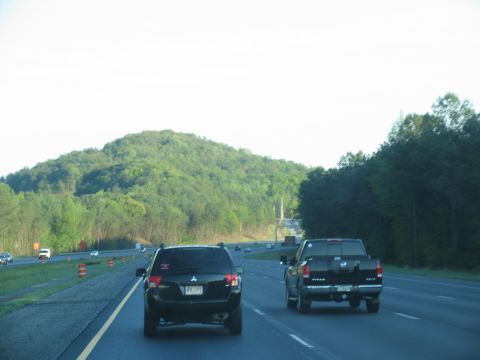1995 Ford C-350 (Centurion Conversions) - Two vehicles travel down a highway with a large, green hill visible in the distance.