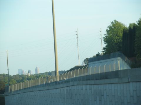 1995 Ford C-350 (Centurion Conversions) - A distant city skyline is visible beyond a concrete barrier and trees under a clear sky.