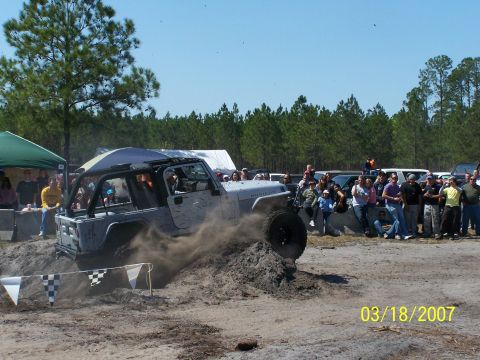 1989 Ford Bronco - A Jeep Wrangler Rubicon navigates an off-road course, with spectators watching in the background.