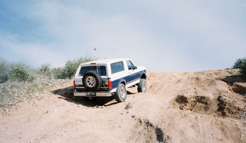 1996 Ford Bronco - A 1996 Ford Bronco navigates a dusty incline under a clear blue sky.