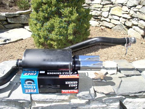 1996 Ford Probe - Aftermarket exhaust muffler with dual chrome tips, supported by tool packaging.