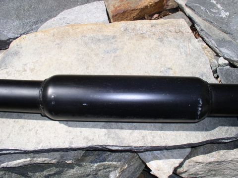 1996 Ford Probe - Close-up of a black exhaust pipe section lying on a bed of rocks.