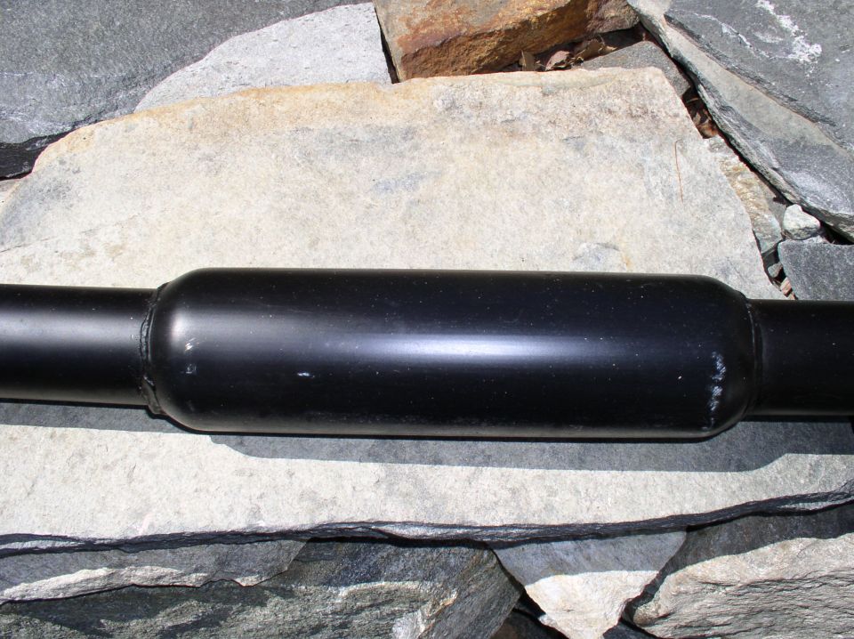 Black exhaust pipe section with a bulge in the middle, resting on rocks