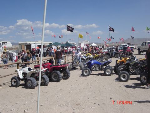 1981 Ford Bronco - A collection of ATVs are parked in a sandy area, with a crowd and various vehicles in the background.