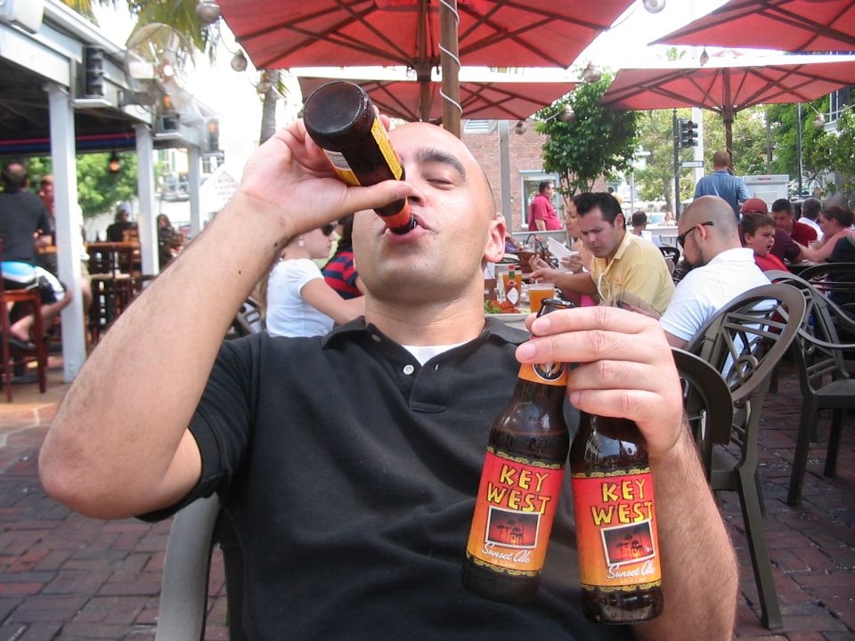 man drinking from a beer bottle, holding another bottle of Key West Sunset Ale