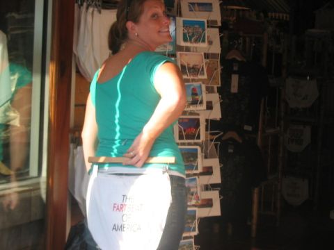 1991 Ford Bronco - A woman displays a humorous novelty item with text on it while standing in front of a postcard rack.