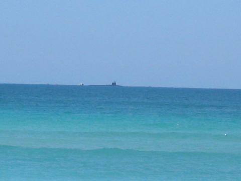 1991 Ford Bronco - A submarine and a barge are visible on the ocean horizon with turquoise waves in the foreground.