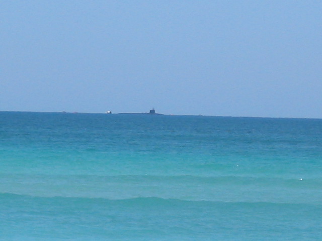 Submarine and barge on the horizon under a clear blue sky