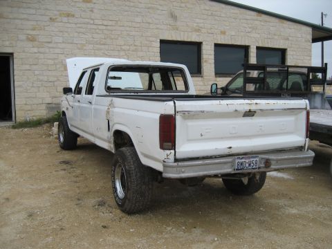 1986 Ford Bronco - This white Ford pickup truck is viewed from the rear, showing its license plate and a slightly damaged tailgate.