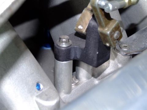 1990 Ford Mustang - A close-up view of an engine component, showing a black bracket and brass lever mechanism.