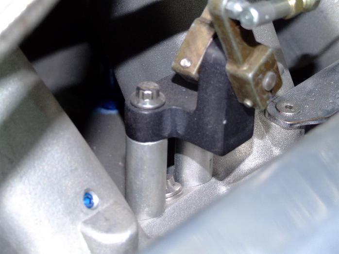 Close-up of a black bracket with a silver bolt and a brass lever attached to an engine component