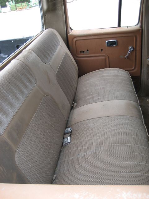 1986 Ford Bronco - The interior of an old vehicle features a faded bench seat and a brown door panel with a manual window crank.