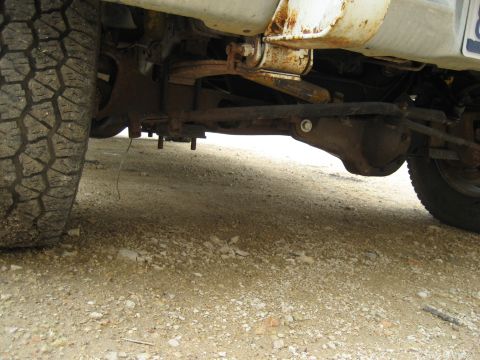 1986 Ford Bronco - The underside of a vehicle, revealing its suspension components and a tire, with visible rust.