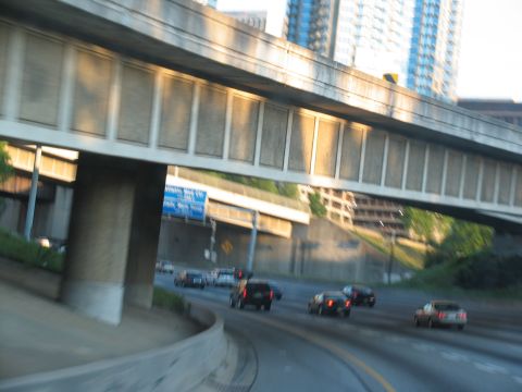 1995 Ford C-350 (Centurion Conversions) - Traffic moves along a highway under a concrete overpass with city buildings visible.