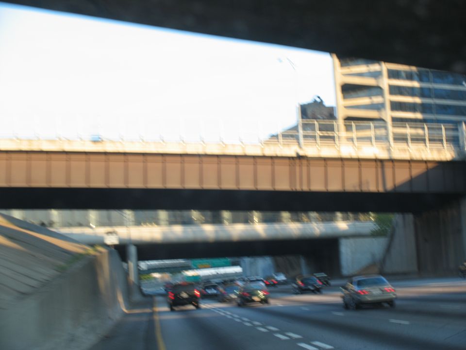 Cars on a highway under an overpass with a tall building in the background
