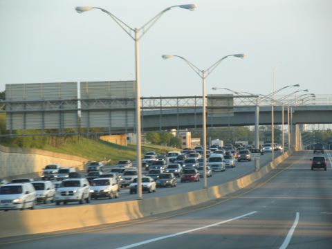 1995 Ford C-350 (Centurion Conversions) - A long line of vehicles are stuck in traffic on a multi-lane highway under an overpass.