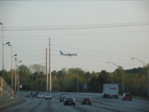 1995 Ford C-350 (Centurion Conversions) - An airplane is seen in the sky above a highway with several cars and a FedEx truck driving on it.