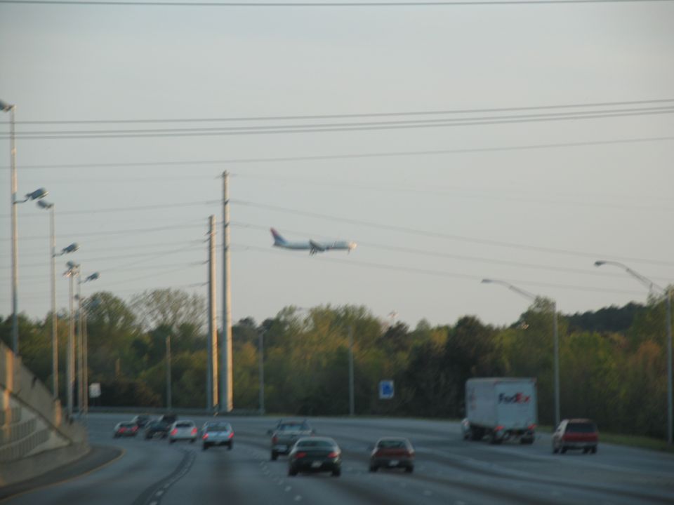 Airplane flying over a highway with cars and a FedEx truck