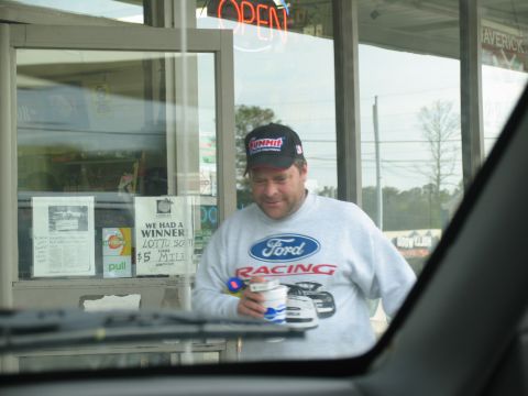1995 Ford C-350 (Centurion Conversions) - Man in Ford Racing sweatshirt and hat holds cups near a store window with lottery signs.
