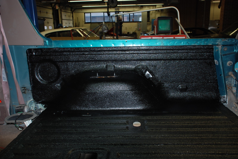 Black spray-in bedliner coating the rear quarter and cargo floor of a stripped teal SUV in a shop