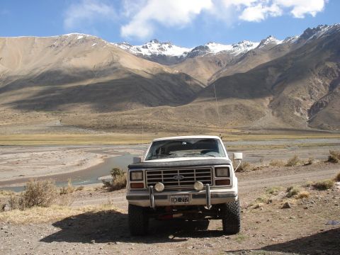 1986 Ford Bronco - A white 1986 Ford Bronco is parked on a dirt road with a river and mountains in the background.