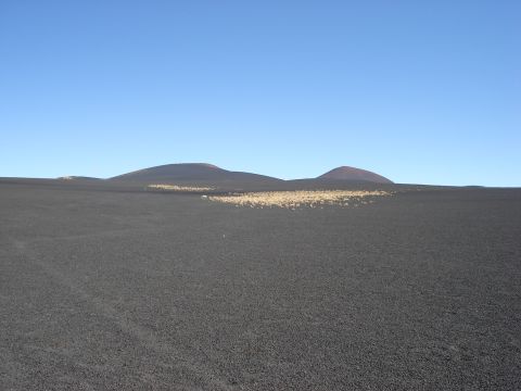 1986 Ford Bronco - A vast, barren landscape stretches out under a bright blue sky, with two volcanic peaks in the distance.
