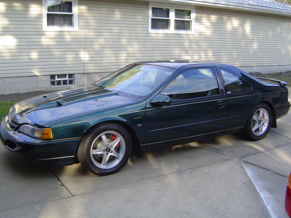 Dark green coupe with hood scoops and red brake calipers, parked on a concrete driveway