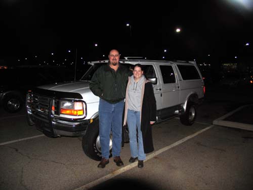 Two people standing in front of a white Ford SUV at night in a parking lot
