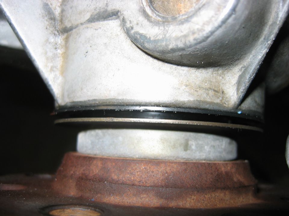 Close-up of metal driveshaft joint with black seals above a rusty flange