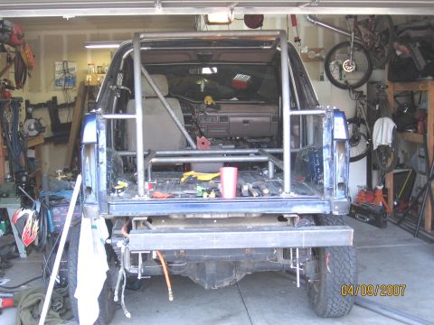 1994 Ford Bronco - The rear of a blue SUV is shown in a garage, modified with a custom metal roll cage.